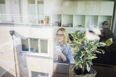 Reife Geschäftsfrau sitzt am Tisch mit einer Tasse Kaffee und schaut aus dem Fenster, lizenzfreies Stockfoto