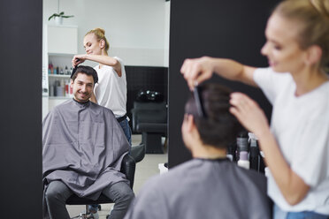 Smiling hairdresser combing man's hair - ABIF00350