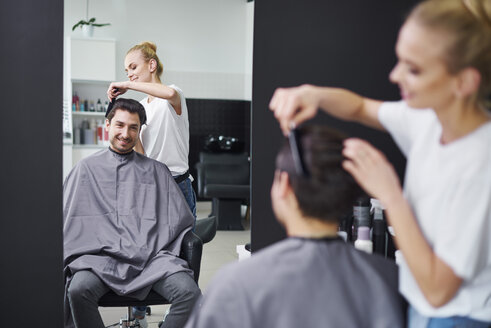 Lächelnder Friseur beim Kämmen der Haare eines Mannes - ABIF00350