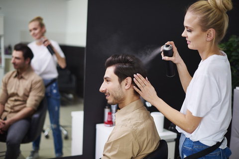 Lächelnder Friseur, der Haarspray auf das Haar eines Mannes sprüht, lizenzfreies Stockfoto