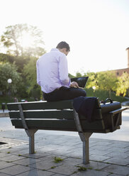 Rear view of man sitting on bench and using laptop - MASF06920