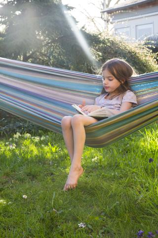 Little girl sitting on hammock in the garden reading a book stock photo