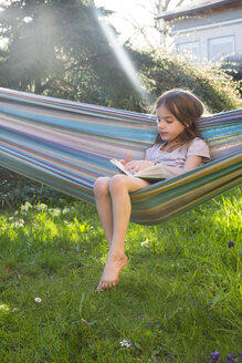 Kleines Mädchen sitzt auf Hängematte im Garten und liest ein Buch - LVF06902