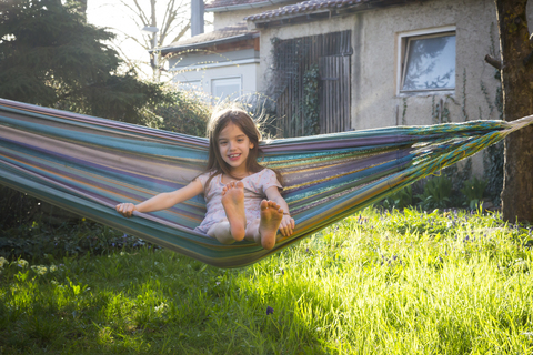 Portrait of smiling little girl sitting on hammock in the garden stock photo