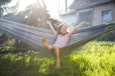 Portrait of happy little girl sitting on hammock in the garden stock photo