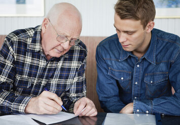 Mann hilft Seniorin beim Ausfüllen eines Formulars - MASF07035