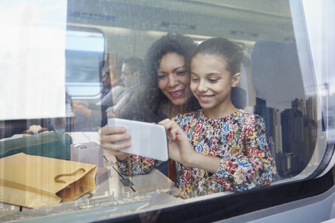 Mutter und Tochter benutzen ein Fotohandy am Fenster eines Personenzugs, lizenzfreies Stockfoto