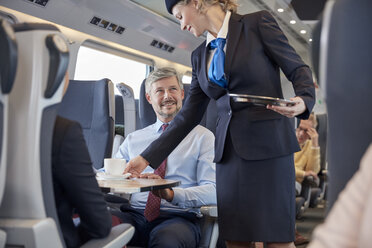 Eine weibliche Zugbegleiterin serviert einem Geschäftsmann im Personenzug Kaffee - CAIF20232