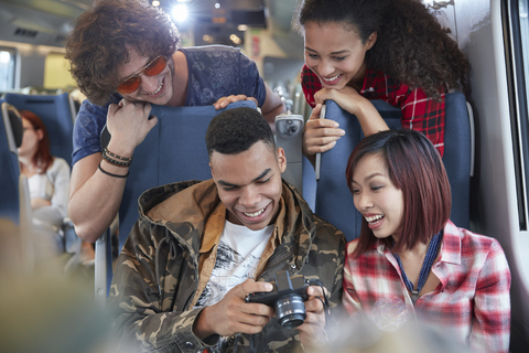 Junge Freunde schauen sich im Personenzug Fotos auf einer Digitalkamera an, lizenzfreies Stockfoto