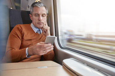 Focused businessman using smart phone at passenger train window - CAIF20239