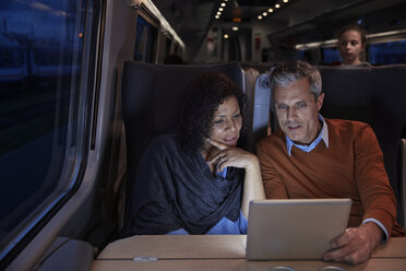 Ehepaar benutzt digitales Tablet in einem dunklen Personenzug bei Nacht - CAIF20244
