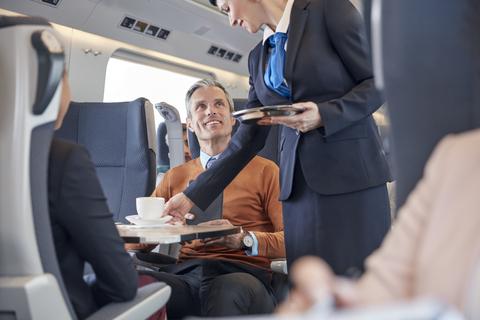 Zugbegleiter serviert einem Geschäftsmann im Personenzug Kaffee, lizenzfreies Stockfoto