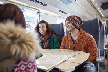 Smiling young friends planning with map on passenger train - CAIF20256