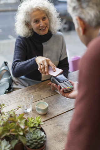 Frau benutzt Smartphone zum kontaktlosen Bezahlen in einem Cafe, lizenzfreies Stockfoto