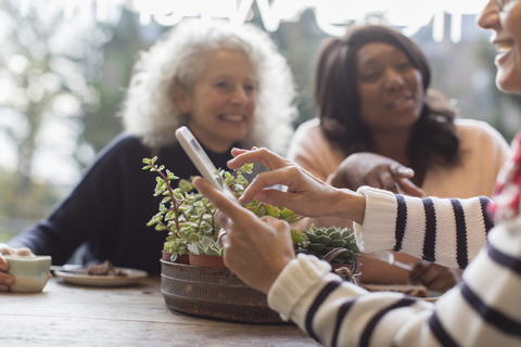 Lächelnde Freundinnen mit Smartphone im Café, lizenzfreies Stockfoto