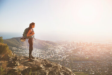 Female rock climber on top of hill overlooking sunny city - CAIF20280