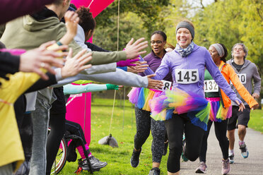 Enthusiastic female runners in tutus high-fiving spectators at charity run in park - CAIF20307