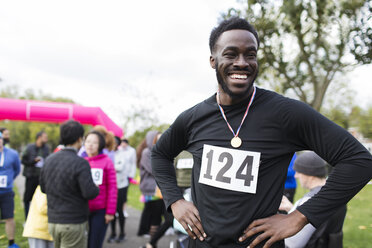 Porträt eines glücklichen, selbstbewussten männlichen Läufers mit Medaille bei einem Wohltätigkeitslauf im Park - CAIF20308
