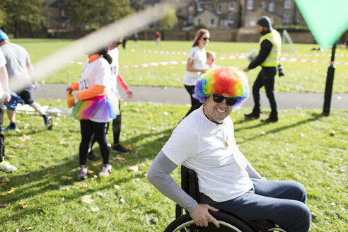 Porträt eines lächelnden, verspielten Mannes im Rollstuhl mit Clownsperücke bei einem Wohltätigkeitsrennen in einem sonnigen Park - CAIF20311