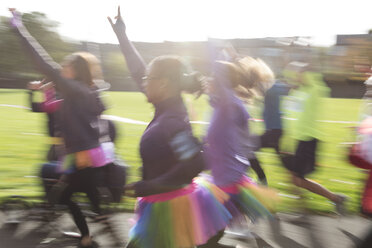 Begeisterte Läufer in Tutus beim Wohltätigkeitslauf im sonnigen Park - CAIF20316