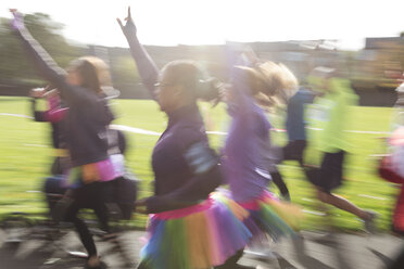 Enthusiastic runners in tutus running at charity run in sunny park - CAIF20316