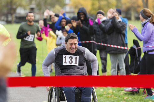 Entschlossener Mann im Rollstuhl nähert sich der Ziellinie eines Wohltätigkeitsrennens im Park - CAIF20336