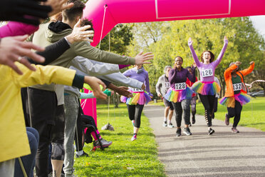 Enthusiastic female runners in tutus nearing finish line at charity run in park - CAIF20340