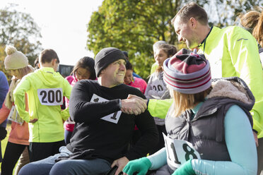 Läufer schüttelt einem Mann im Rollstuhl beim Wohltätigkeitslauf im sonnigen Park die Hand - CAIF20343