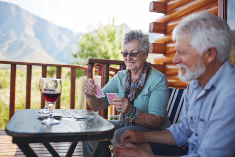 Aktives Seniorenpaar trinkt Wein und spielt Karten auf dem Kabinenbalkon, lizenzfreies Stockfoto