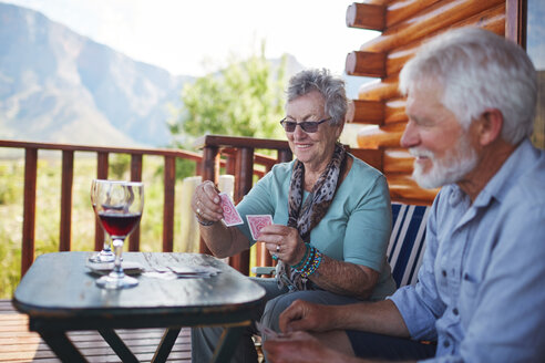 Active senior couple drinking wine and playing cards on cabin balcony - CAIF20370