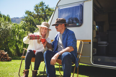 Aktives älteres Paar trinkt Kaffee vor einem Wohnmobil auf einem sonnigen Sommercampingplatz - CAIF20377