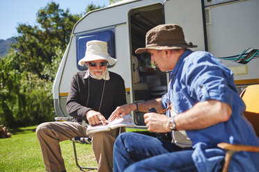 Ältere Männer, die sich vor einem Wohnmobil auf einem sonnigen Sommercampingplatz einen Reiseführer ansehen - CAIF20381