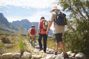 Active senior friends with backpacks hiking along sunny summer footpath - CAIF20384