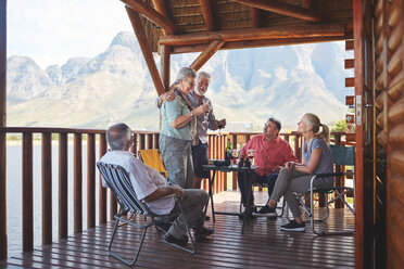 Aktives Seniorenpaar stößt mit Freunden auf dem Balkon einer Hütte am See mit Weingläsern an - CAIF20386