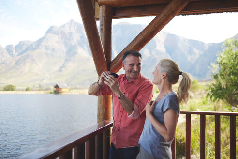 Glückliches Paar mit Fernglas genießt den Seeblick vom Balkon aus - CAIF20390