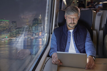 Man using digital tablet on passenger train at night - CAIF20398