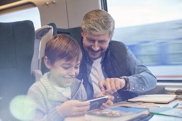 Father and son using smart phone on passenger train - CAIF20399