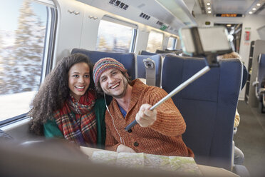 Happy young couple taking selfie with selfie stick on passenger train - CAIF20405