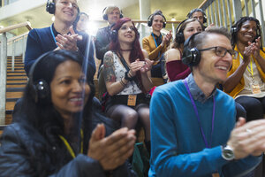 Lächelndes Publikum mit Kopfhörern, das bei einer Konferenz klatscht - CAIF20418