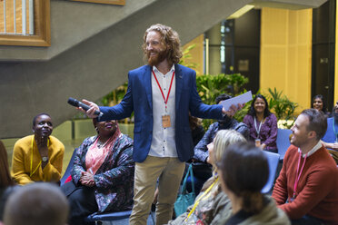 Smiling male speaker with microphone talking to conference audience - CAIF20448