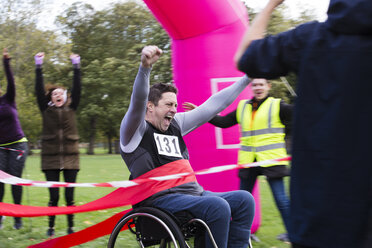 Enthusiastischer Mann im Rollstuhl beim Überqueren der Ziellinie eines Wohltätigkeitsrennens - CAIF20460