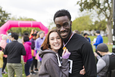 Portrait glückliches Paar Läufer mit Medaille bei Wohltätigkeitslauf im Park - CAIF20500