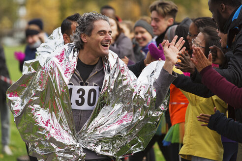 Enthusiastischer männlicher Marathonläufer in Thermodecke, der den Zuschauern zujubelt - CAIF20505