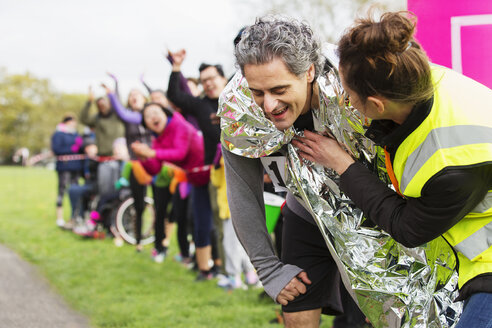 Frau wickelt Wärmedecke um erschöpften männlichen Läufer im Ziel des Marathons - CAIF20509