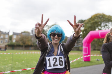Porträt einer begeisterten Läuferin mit Perücke, die bei einem Wohltätigkeitslauf im Park ein Friedenszeichen macht - CAIF20514