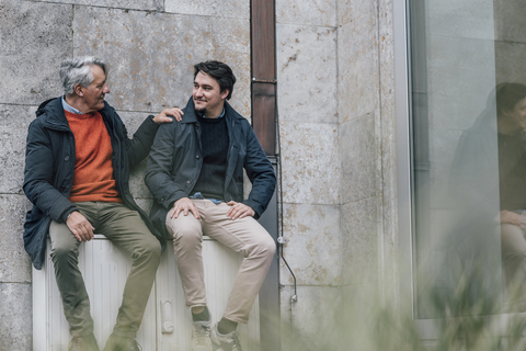 Selbstbewusster älterer Mann und junger Mann sitzen in der Stadt und unterhalten sich, lizenzfreies Stockfoto