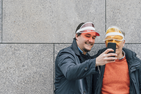 Lächelnder junger Mann und älterer Mann mit Sonnenblende machen ein Selfie, lizenzfreies Stockfoto