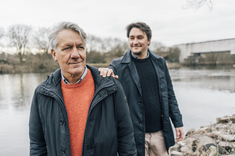 Selbstbewusster älterer Mann und junger Mann am Flussufer stehend, lizenzfreies Stockfoto