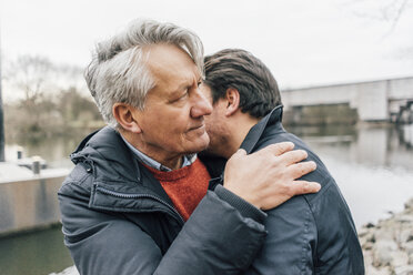 Young man and senior man embracing at the riverside - GUSF00659