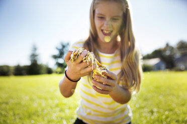 Happy girl holding pumpkin pulp on field during summer - CAVF48175